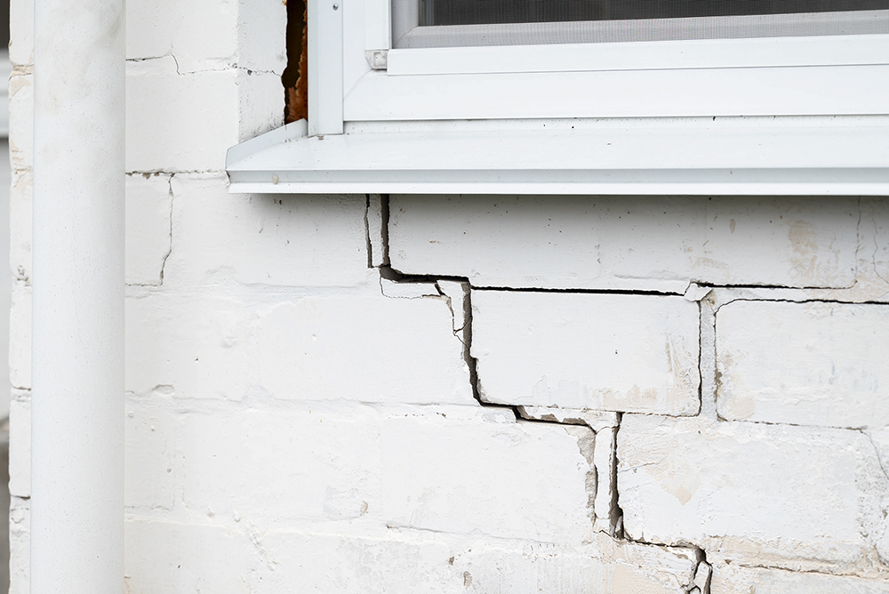Cracked brick wall of private house. Crack under the window on white brick wall, problems with foundation