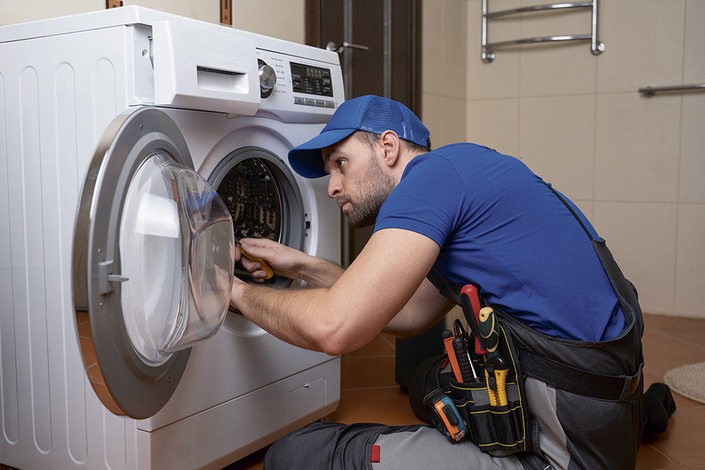 Working man plumber repairs a washing machine in home. Washing machine installation or repair. plumber connecting appliance